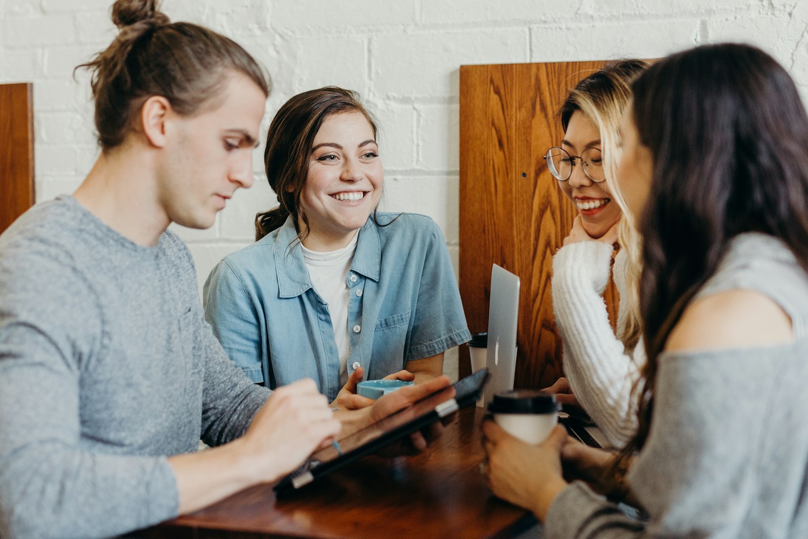 Four students smiling and talking over coffee and a tablet.